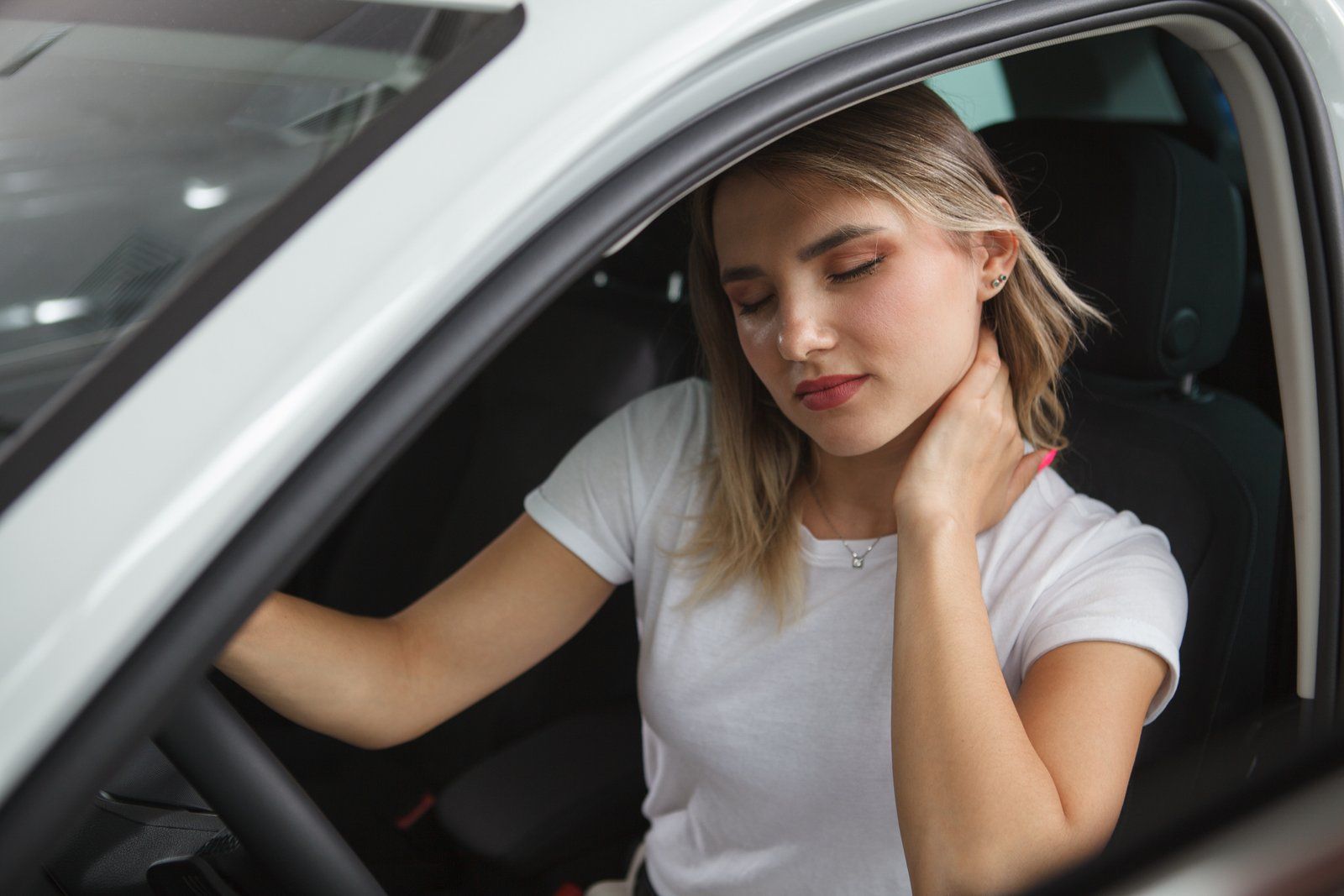 Woman seated in a white car holding her neck